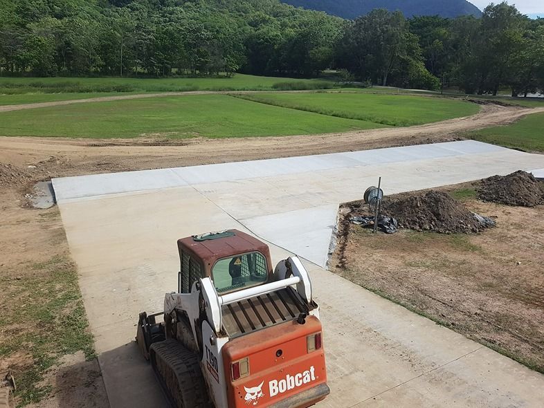 A Bobcat Tractor Is Parked In A Driveway Next To A Field — B & C Donnachie Concrete Contractors in Kuranda, QLD
