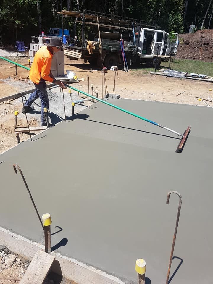 A Man Is Spreading Concrete On A Construction Site With A Broom — B & C Donnachie Concrete Contractors in Kuranda, QLD