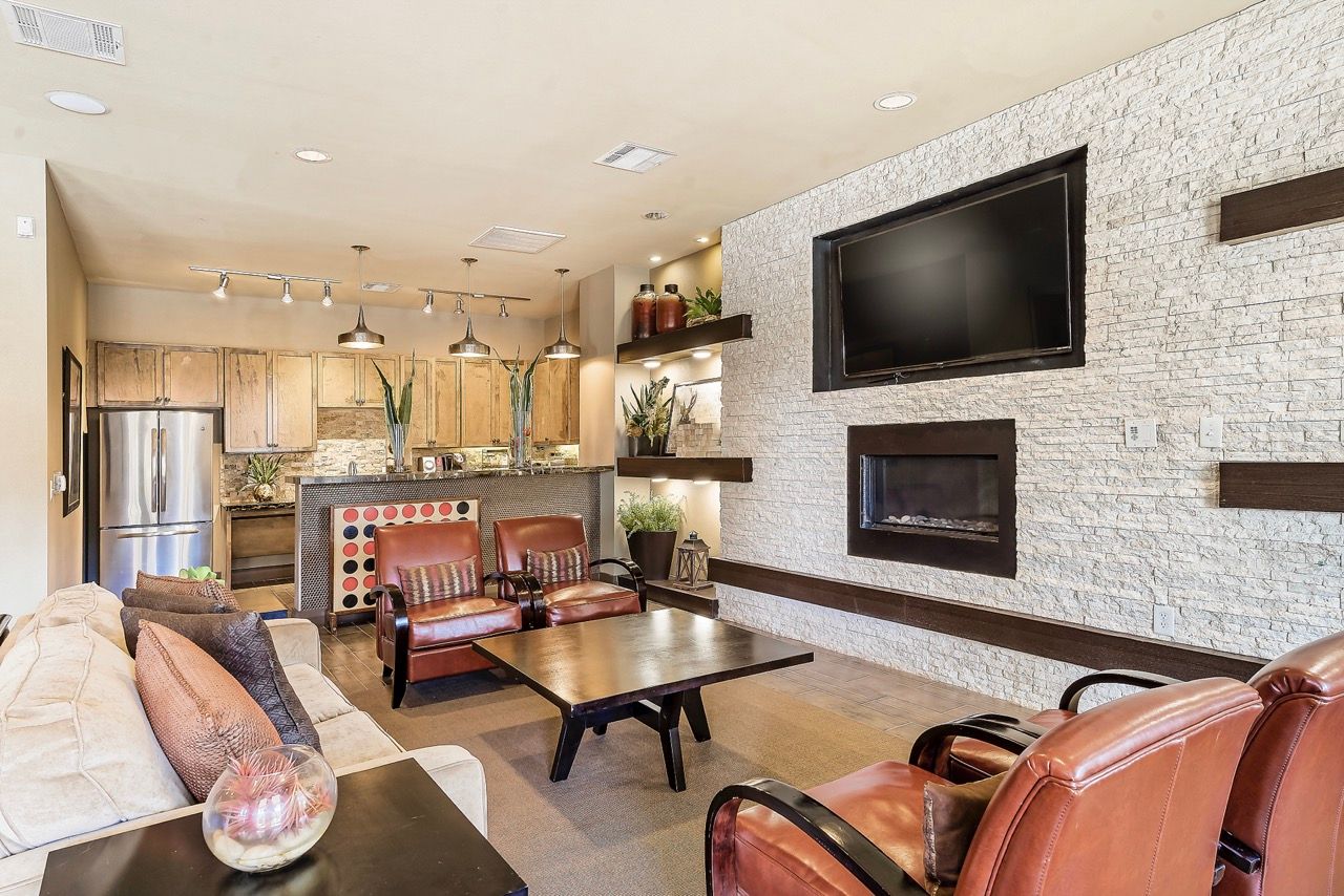 Modern communal living area with beige sofa, leather chairs, coffee table, fireplace, and wall-mounted TV.