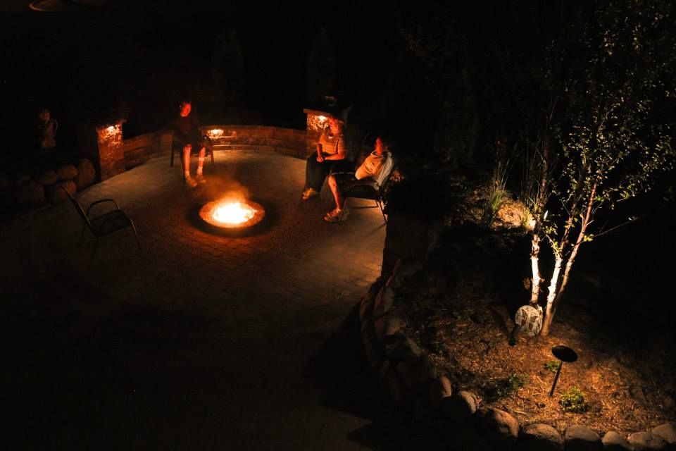 A Group Of People Are Sitting Around A Fire Pit At Night — Menasha, WI — Artscapes COC