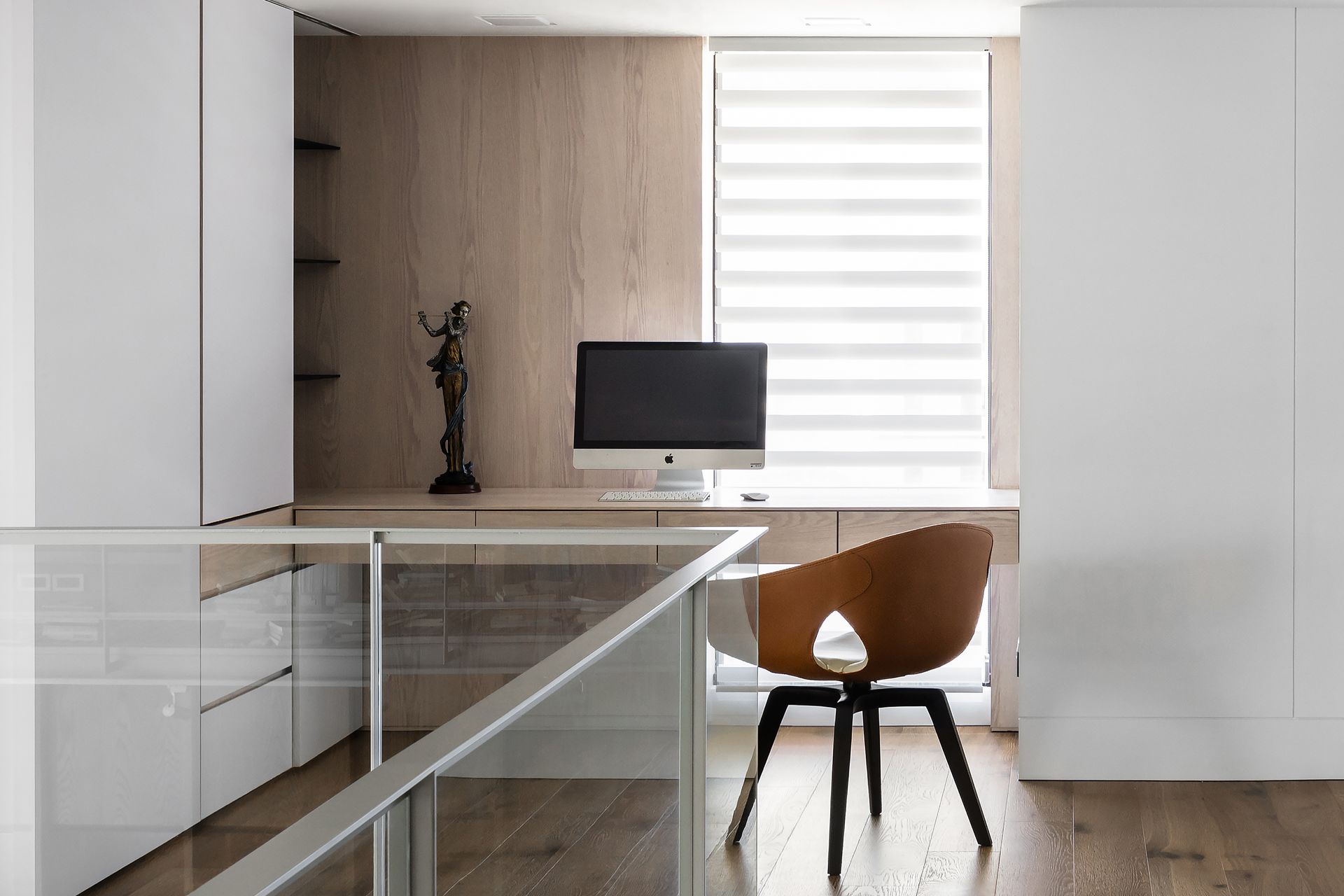 Modern home office with wood and white accents, featuring a desk, chair, and computer near a window.