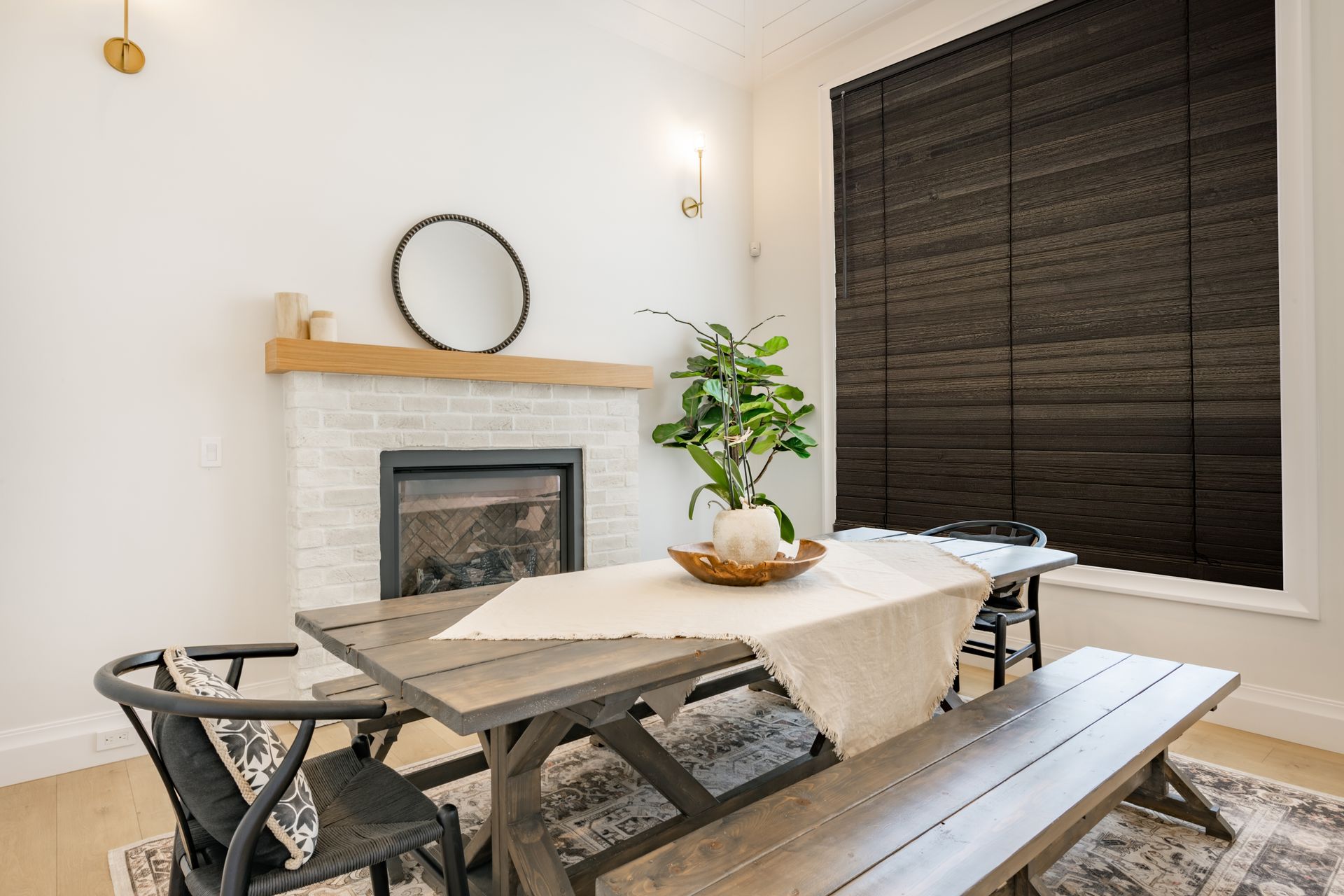 Dining room with gray table, bench, chair, fireplace, and dark brown window shade.