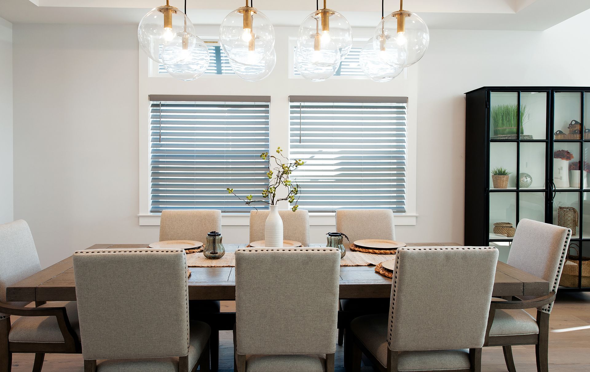 Dining room with a wooden table and six upholstered chairs, under three pendant lights.