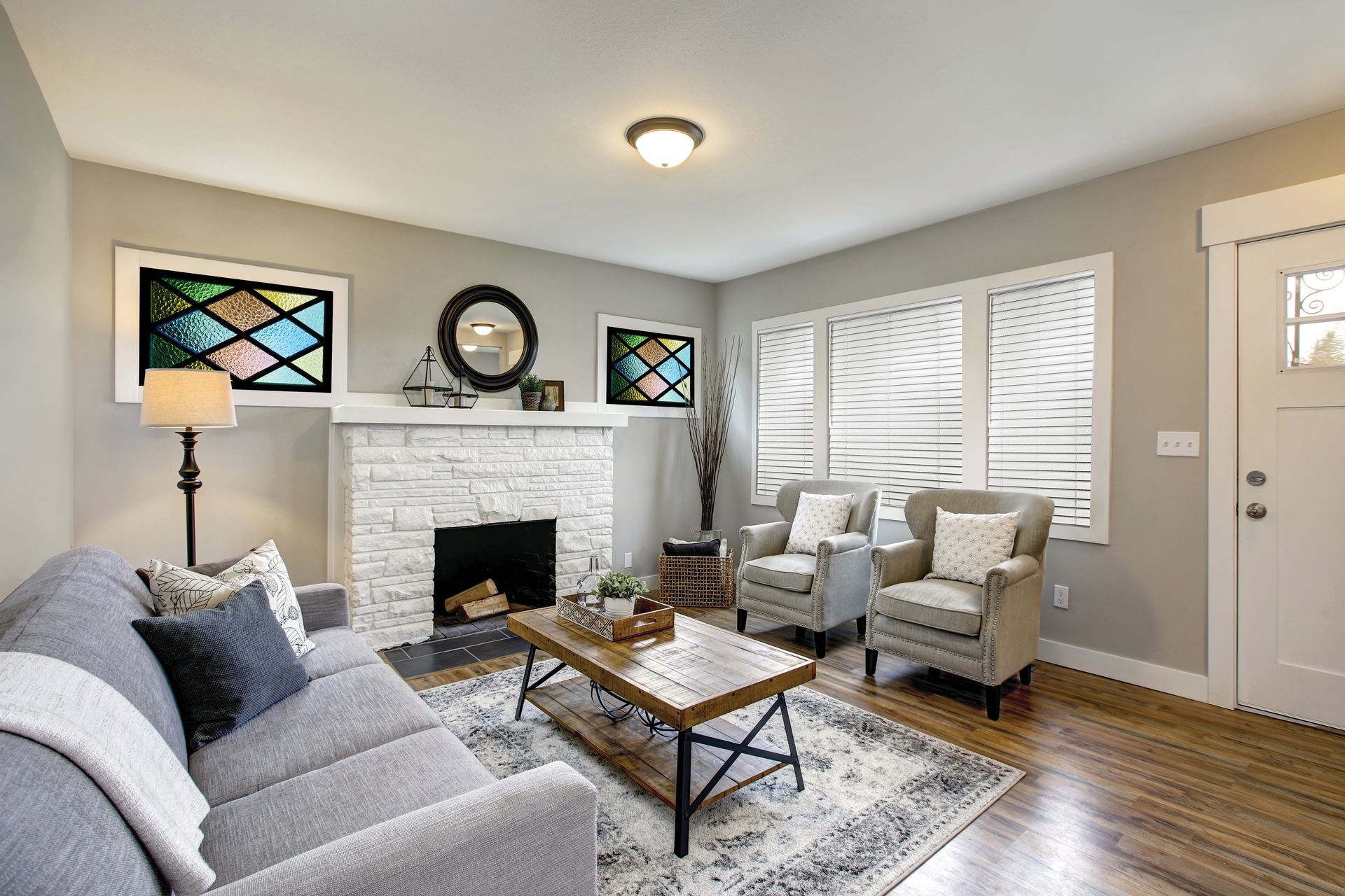 Living room with gray sofa, white brick fireplace, armchairs, coffee table, and wood floors.