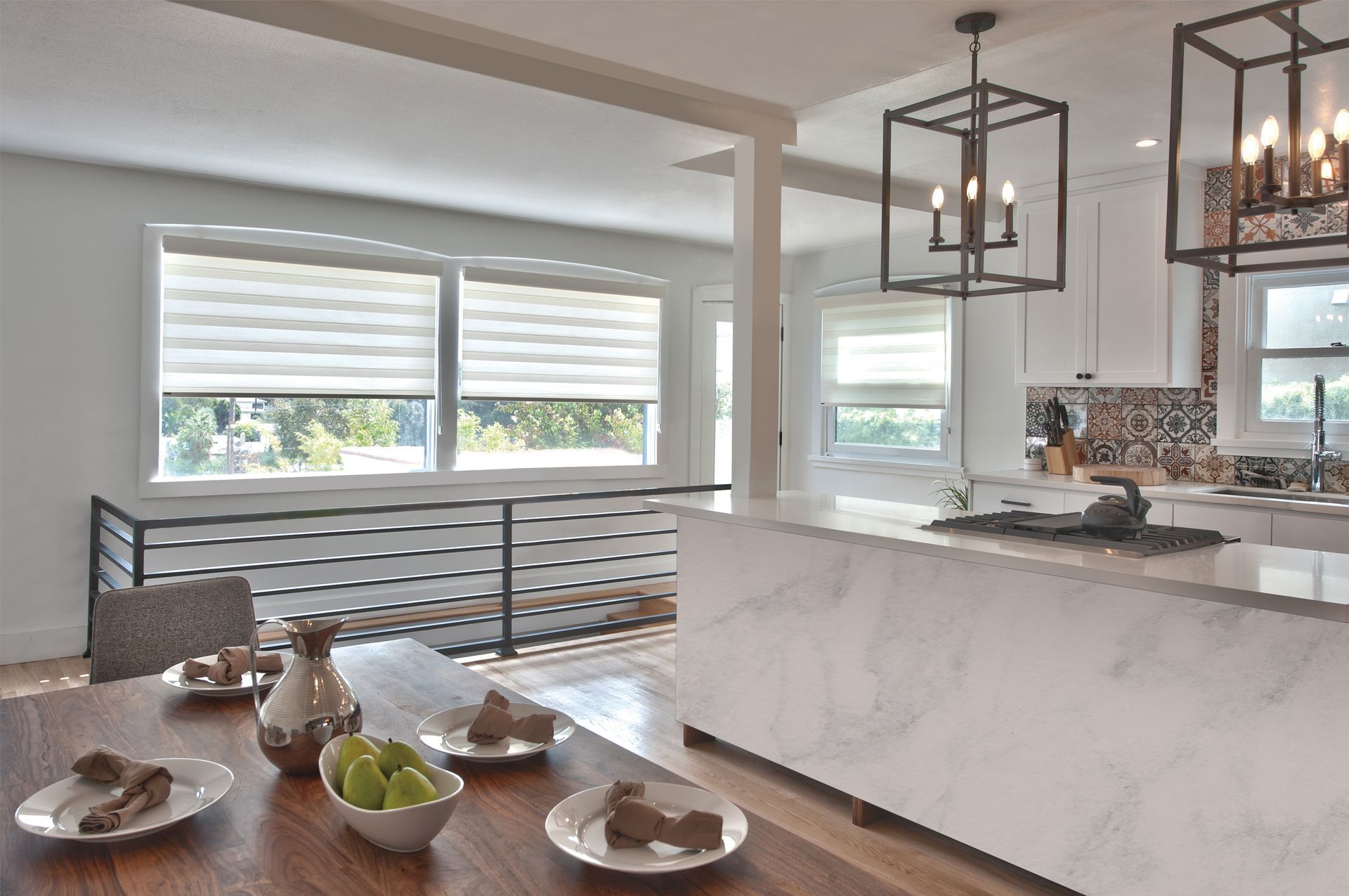 Interior view of a kitchen and dining area with a wooden table set for a meal. Windows and countertops.
