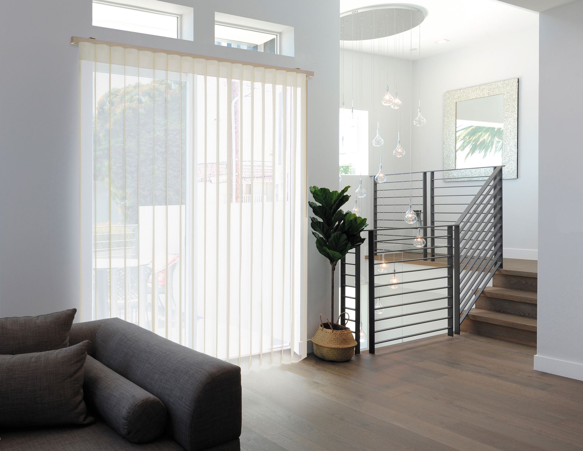 Living room with vertical blinds, gray sofa, and stairs.