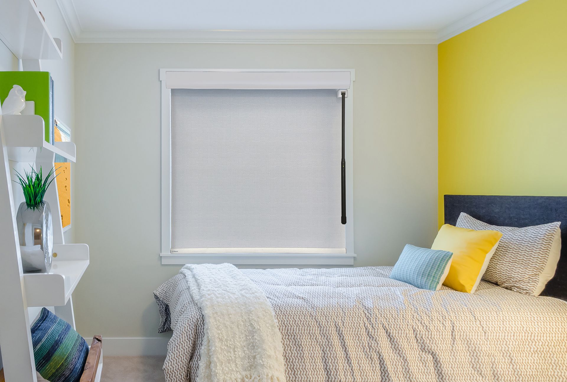 Bedroom with bed, window with blind, shelves on wall, and yellow accent wall.