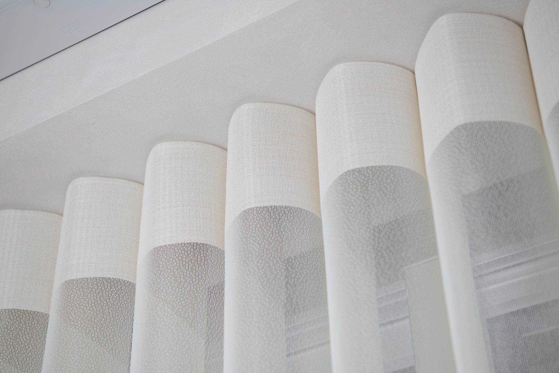White, textured curtains hanging from a ceiling track, creating soft folds.