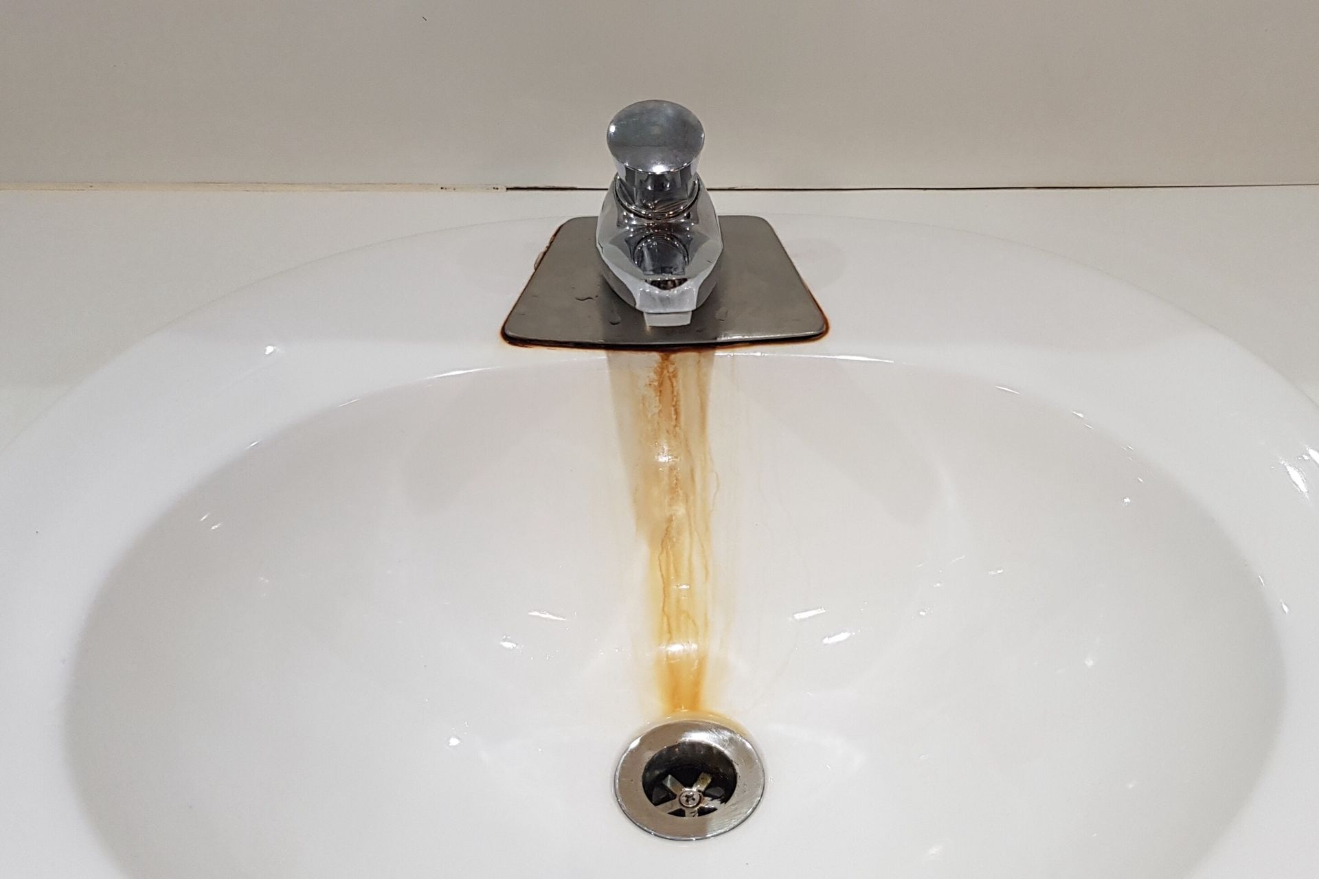 A white sink with a rusty faucet and drain