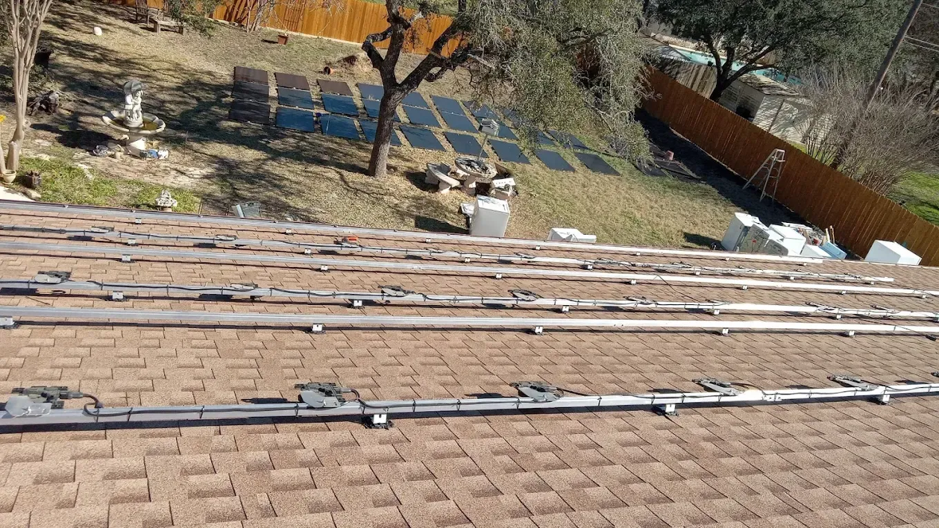Brown shingle roof with solar panel mounting rails visible; background shows solar panels on a hillside.