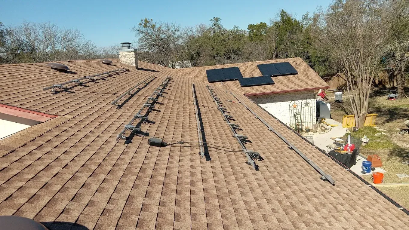 Brown shingled roof with solar panels and roof mount rails on a sunny day.