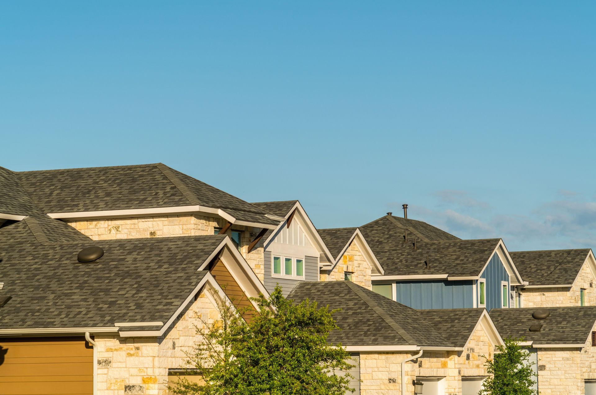 Row of houses with gray shingled roofs and light-colored stone exteriors against a blue sky.