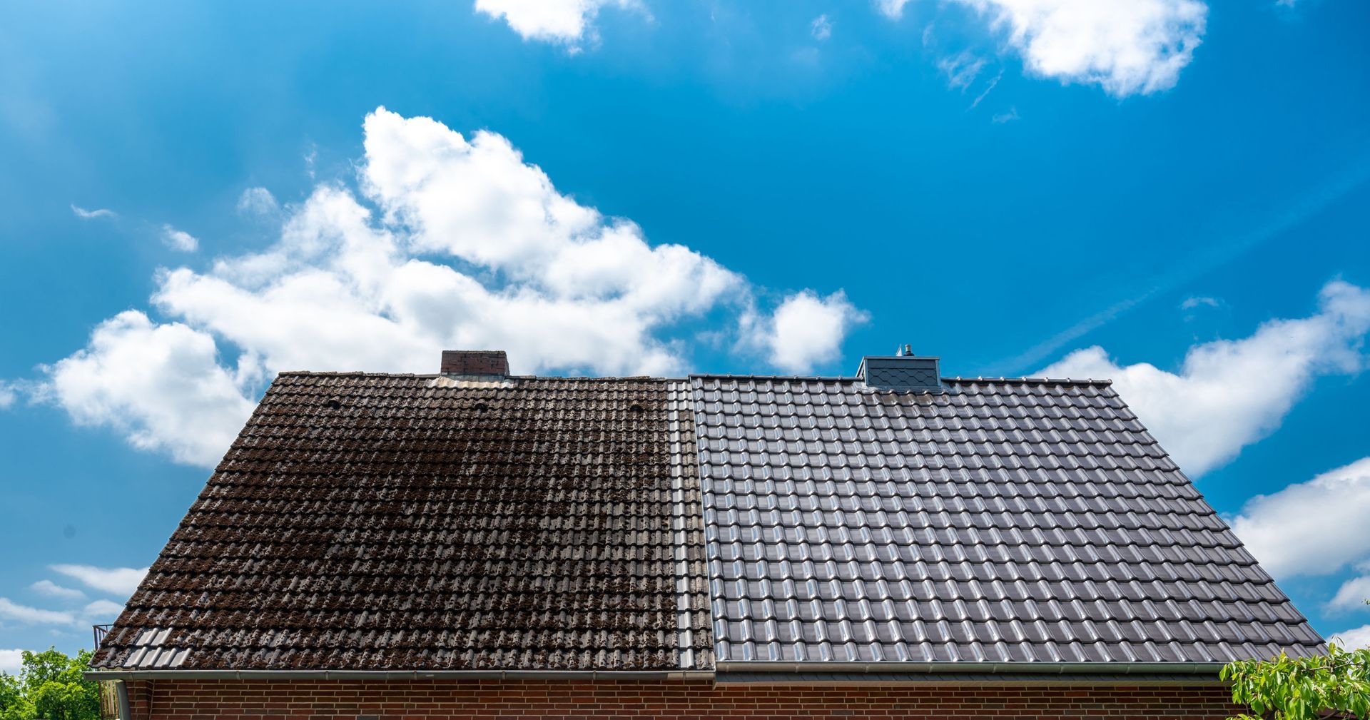 Roof half cleaned, half dirty against a blue sky with clouds.