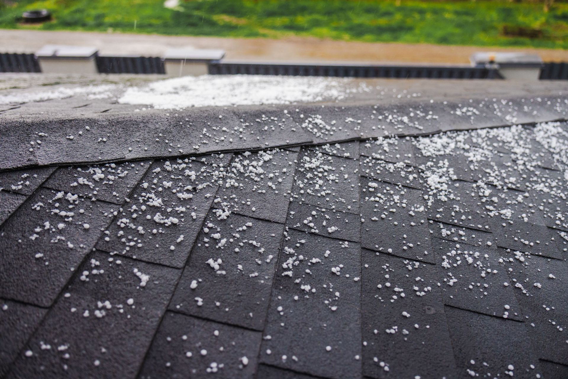 Hail covering a black asphalt shingle roof during a storm.