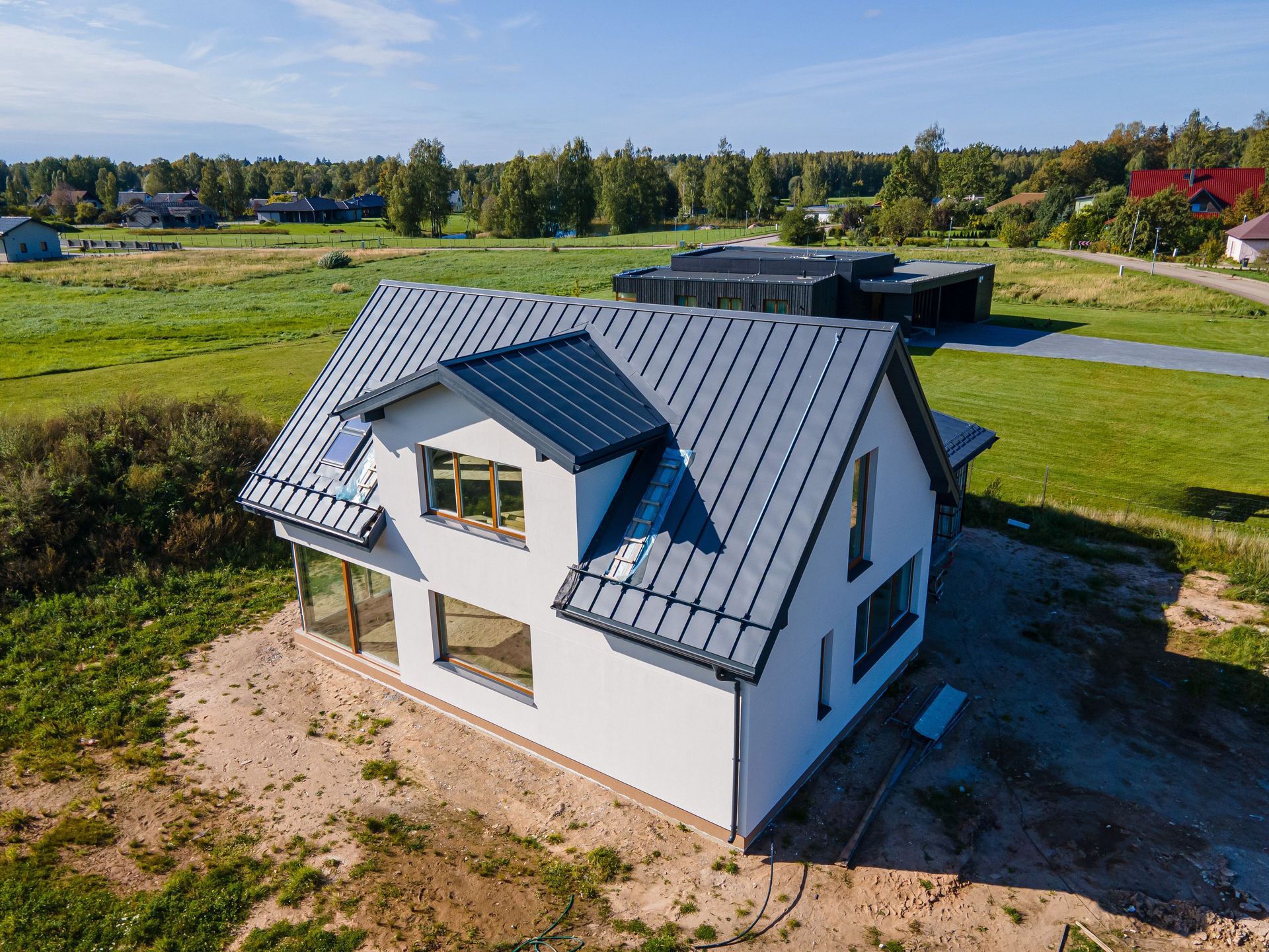 Modern two-story white house with gray roof, large windows, and dormers, on a grassy plot.
