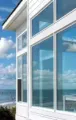 Modern white beachfront house with large windows overlooking the ocean and blue sky