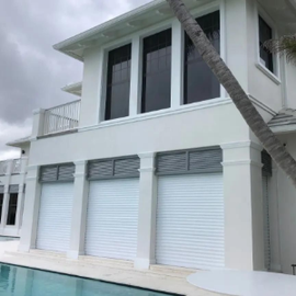 Two-story white house with rolling storm and security shutters installed on the lower level.