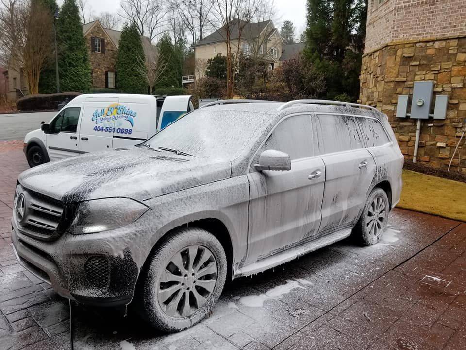A mercedes benz suv is covered in foam in a driveway.