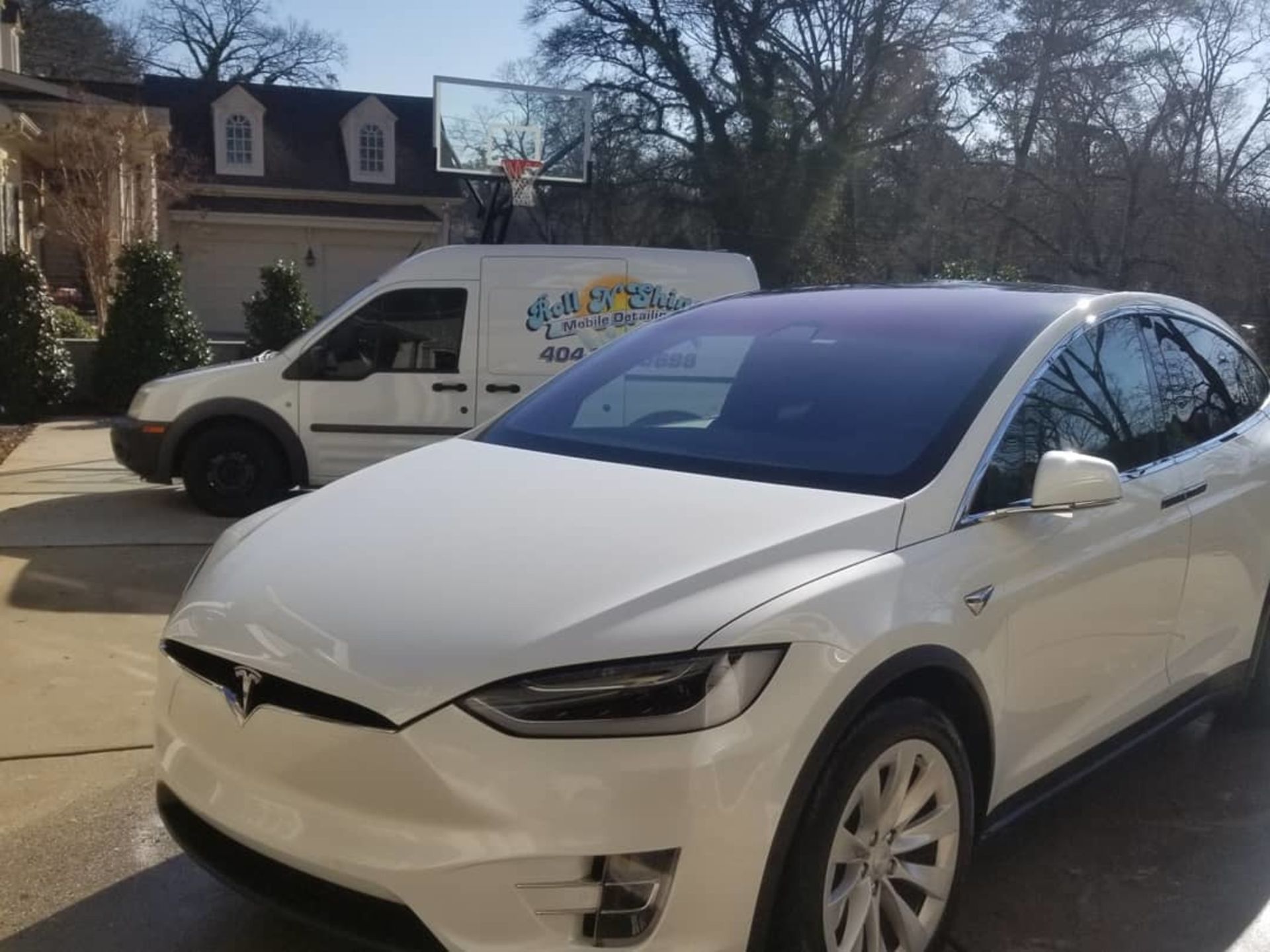 A white tesla model x is parked in a driveway next to a white van.