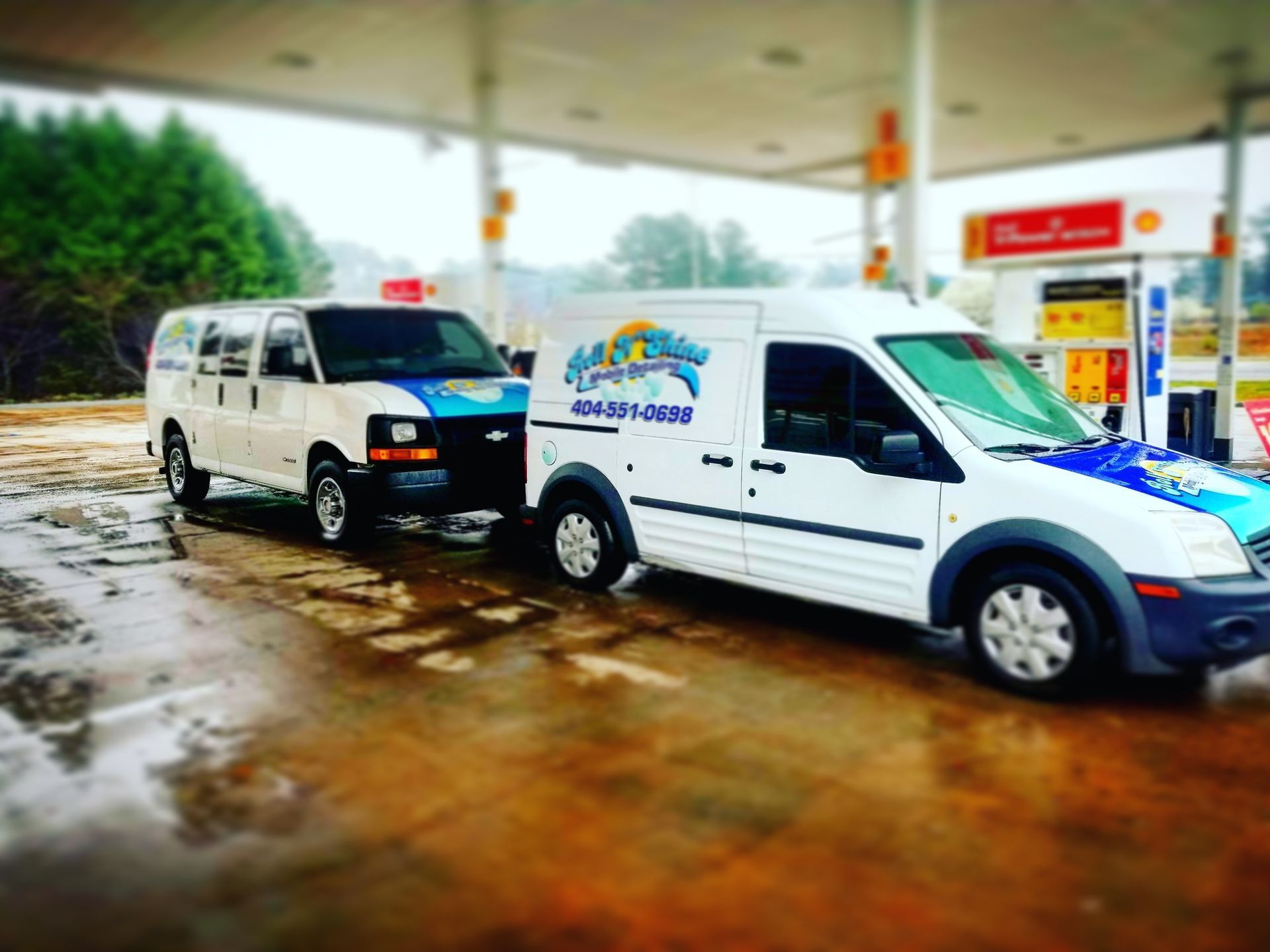 Two white vans are parked next to each other at a gas station.