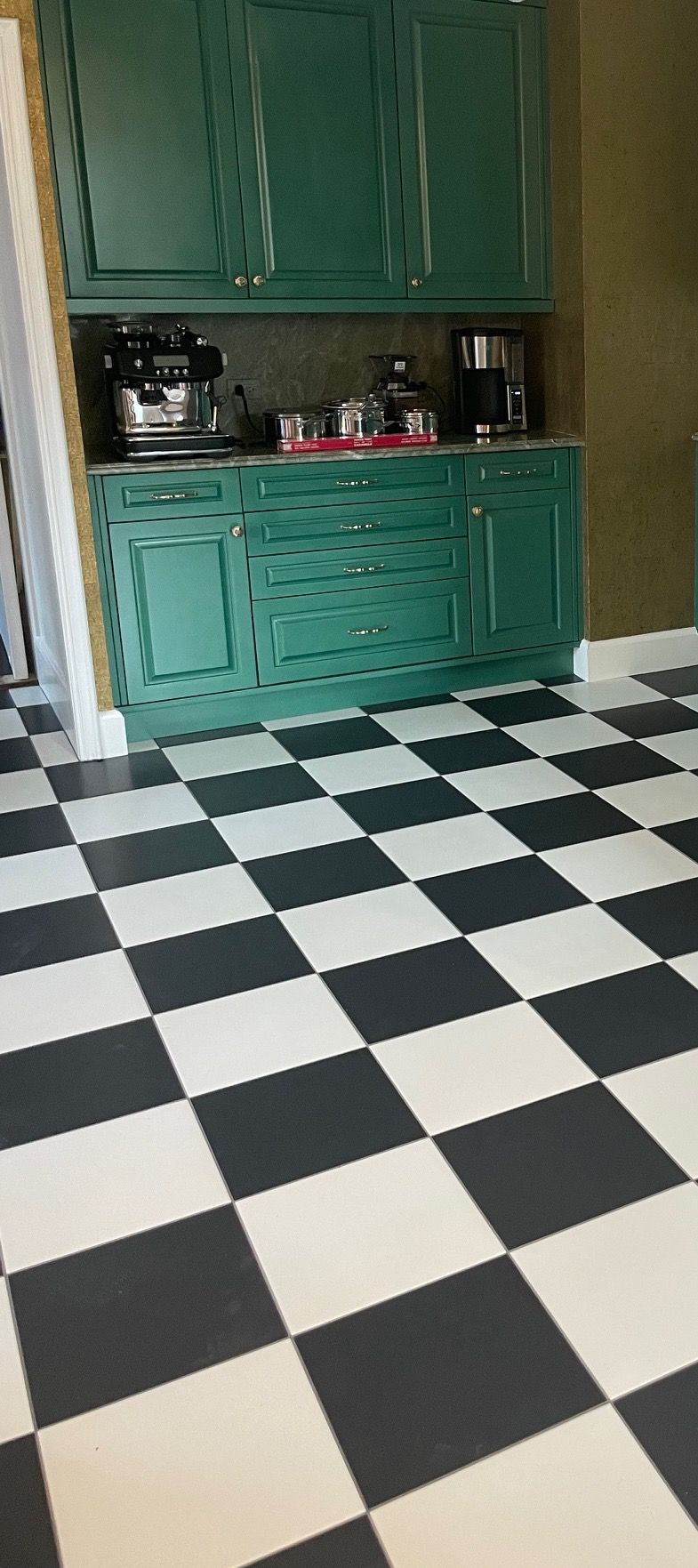 A black and white checkered floor in a kitchen with green cabinets.