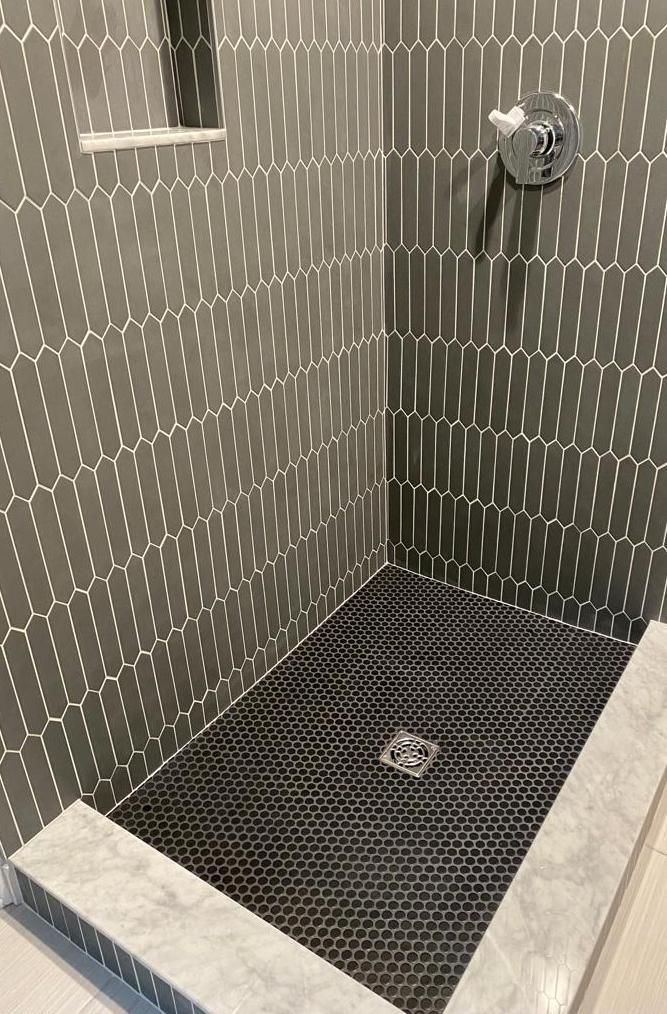 A walk in shower with gray tiles and a black tile floor.