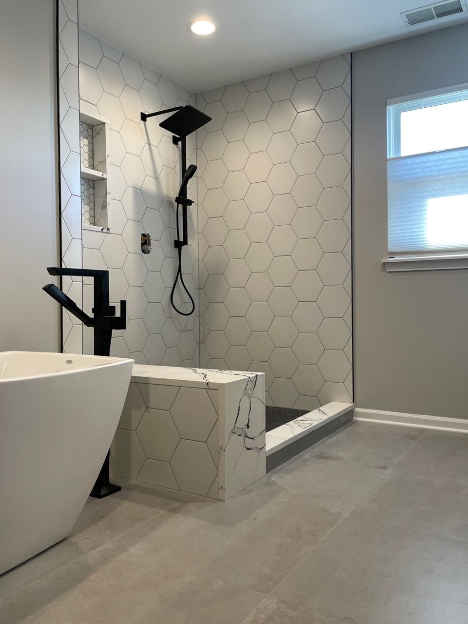 A bathroom with a tub , sink , shower and window.