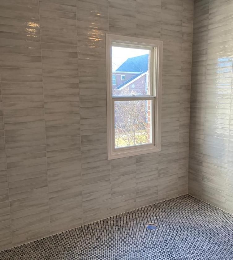 A bathroom with white tile walls and a window.