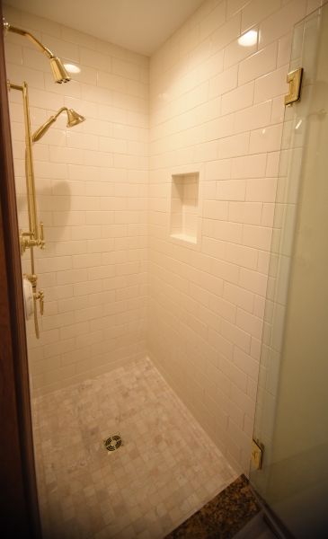 A walk in shower with two shower heads and a glass door.