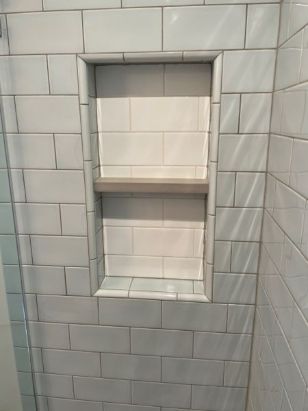 A shower with white tiles and a shelf in it.
