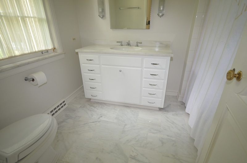 A bathroom with a toilet , sink , mirror and window.