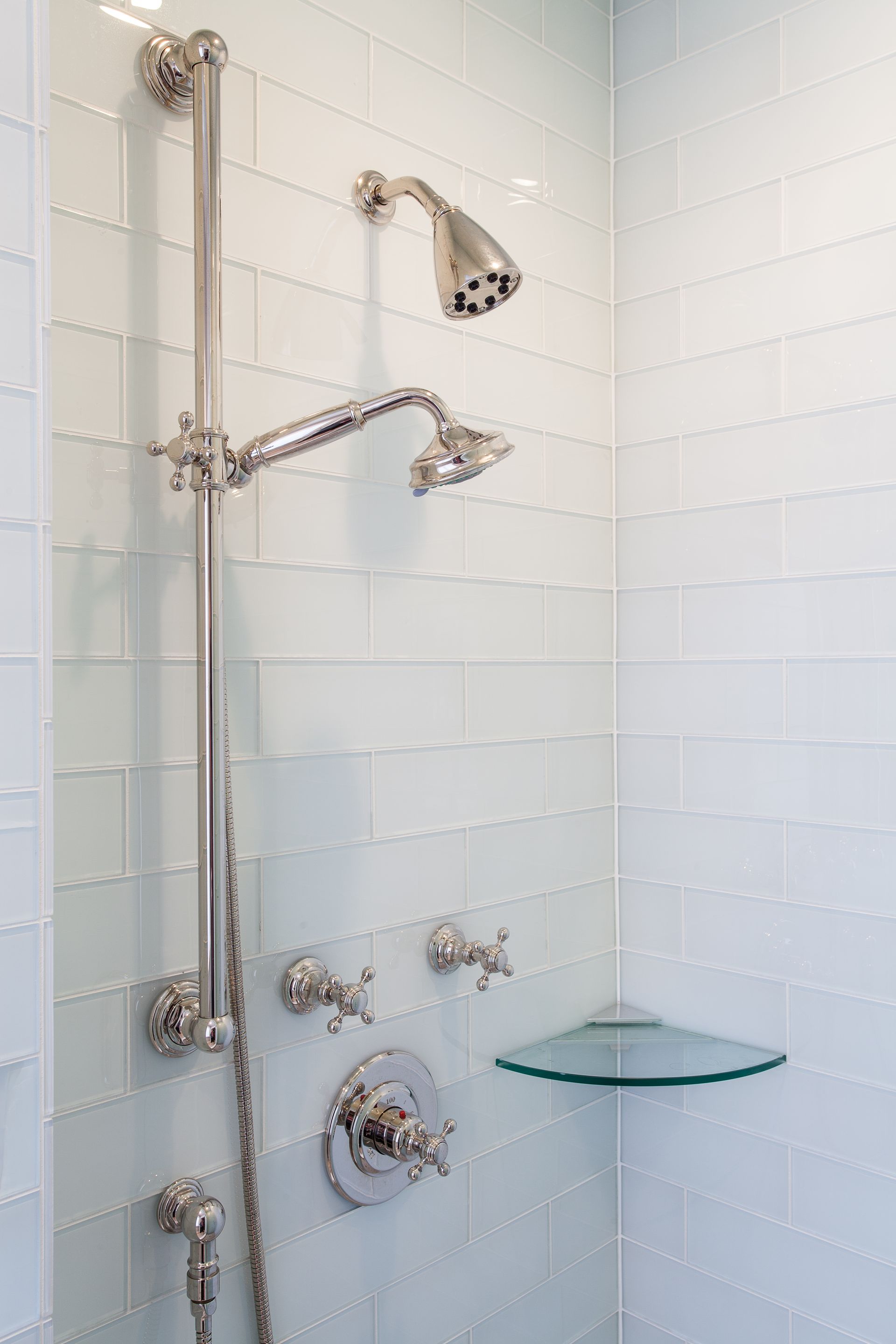 A shower with two shower heads and a glass shelf.