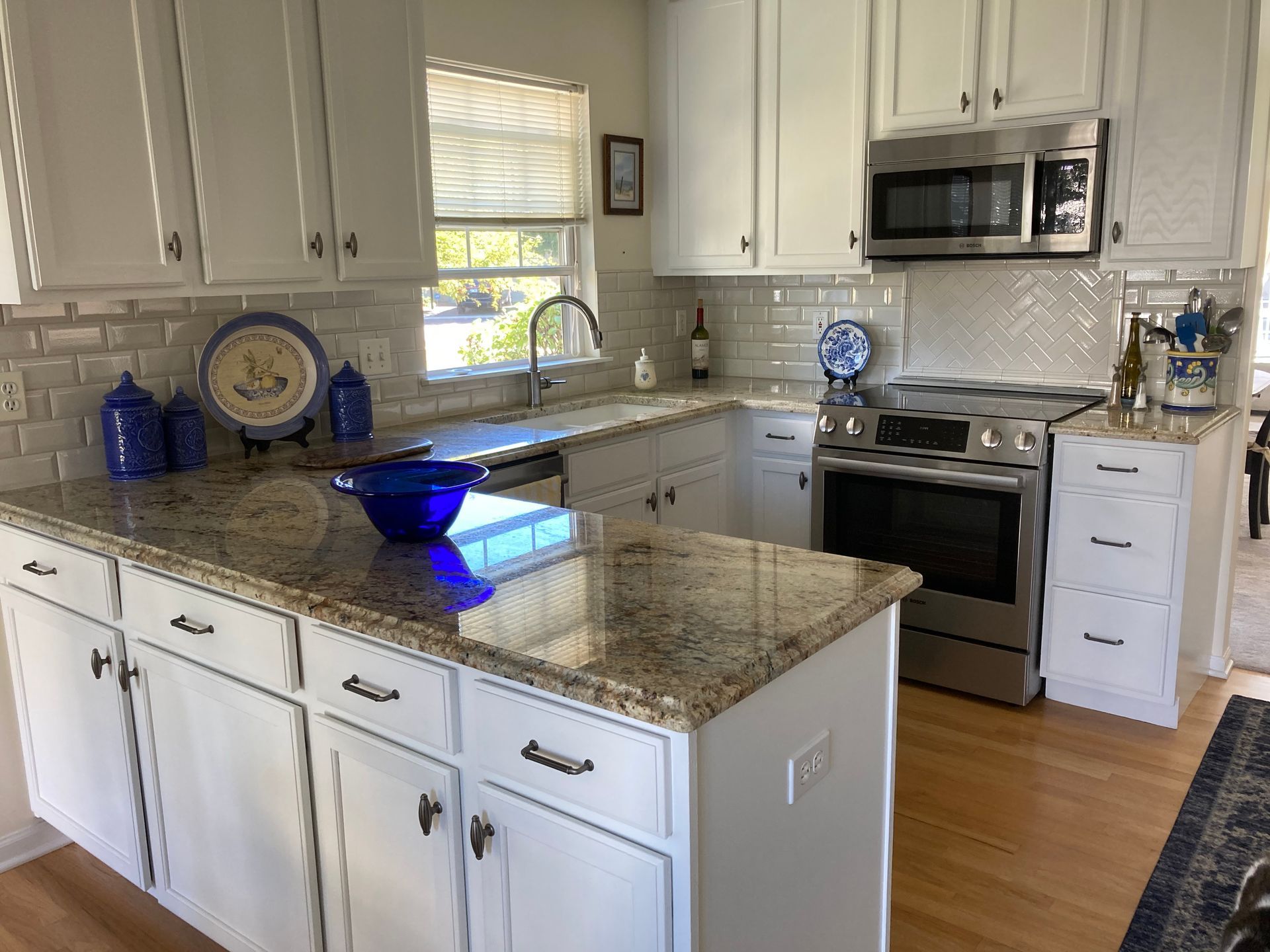 A kitchen with white cabinets , granite counter tops , stainless steel appliances and a large island.