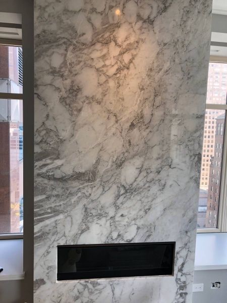 There is a fireplace in the middle of a marble wall.