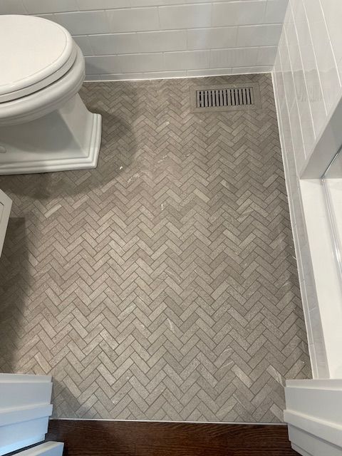 A bathroom with a toilet and a herringbone tile floor.