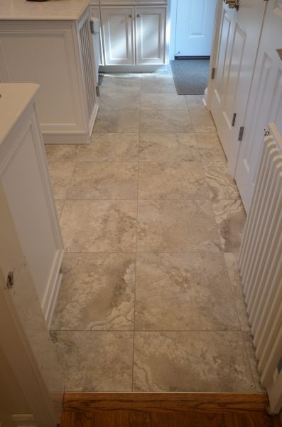 A tiled floor in a kitchen with white cabinets and a radiator.