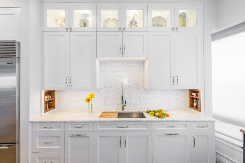A kitchen with white cabinets , a sink , a refrigerator , and a window.