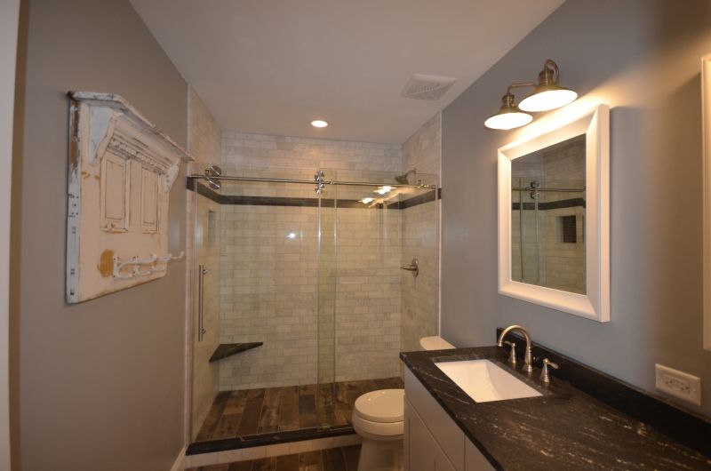 A bathroom with a walk in shower , sink , toilet and mirror.