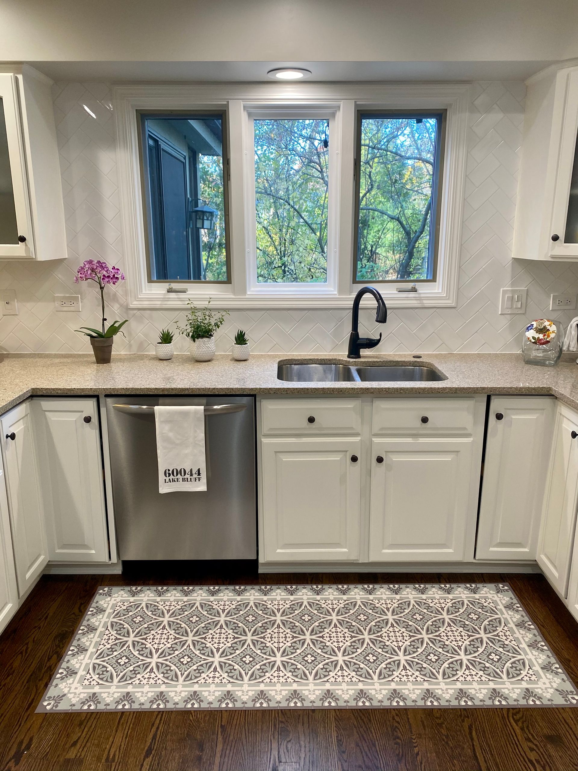 A kitchen with white cabinets , a stainless steel dishwasher , a sink , and a window.