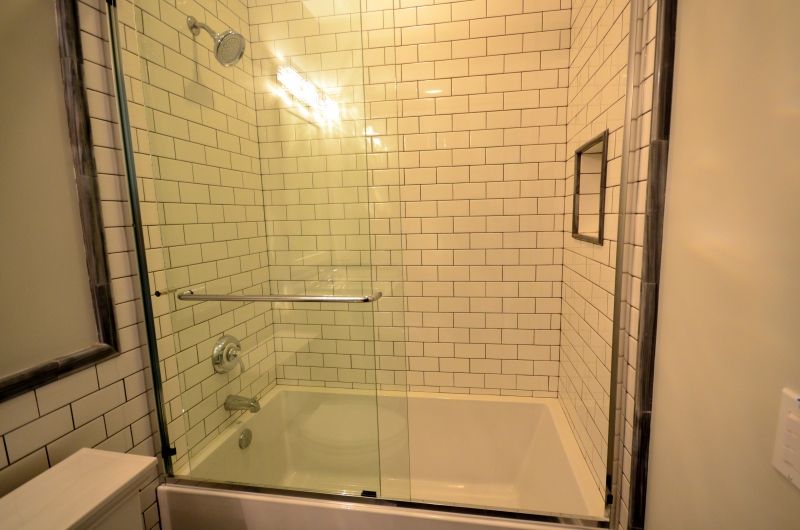 A bathroom with white brick walls and a bathtub with a glass shower door.