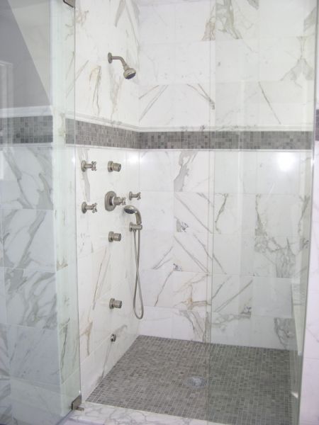 A walk in shower with marble walls and a glass door