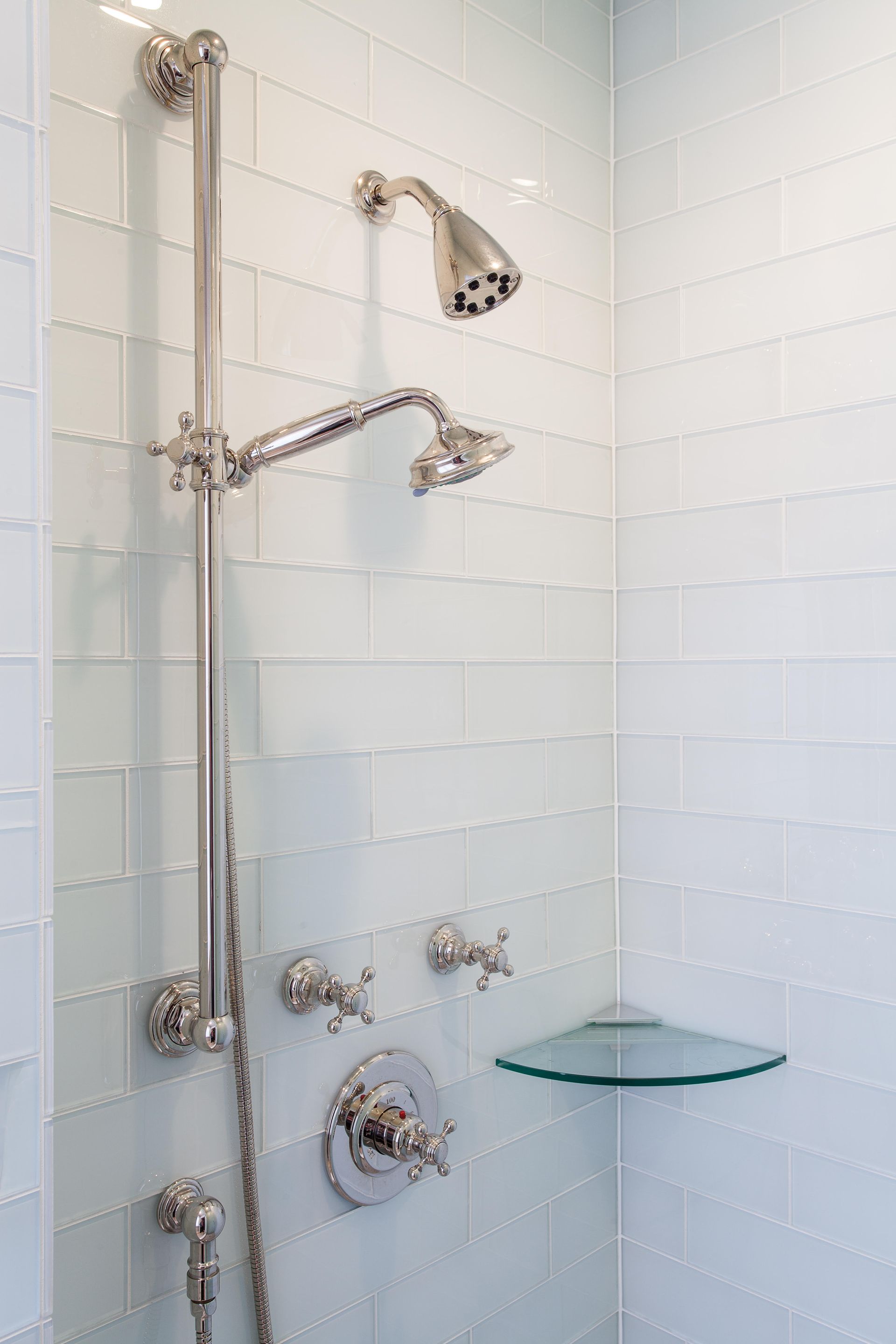 A shower with two shower heads and a glass shelf.