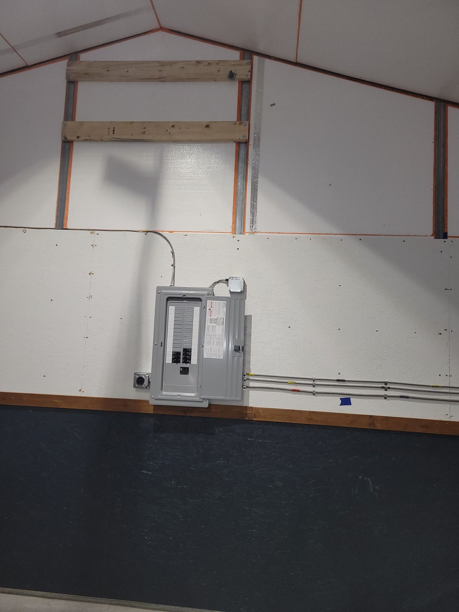 Gray electrical panel mounted on a white and black wall. Brown wooden framing.