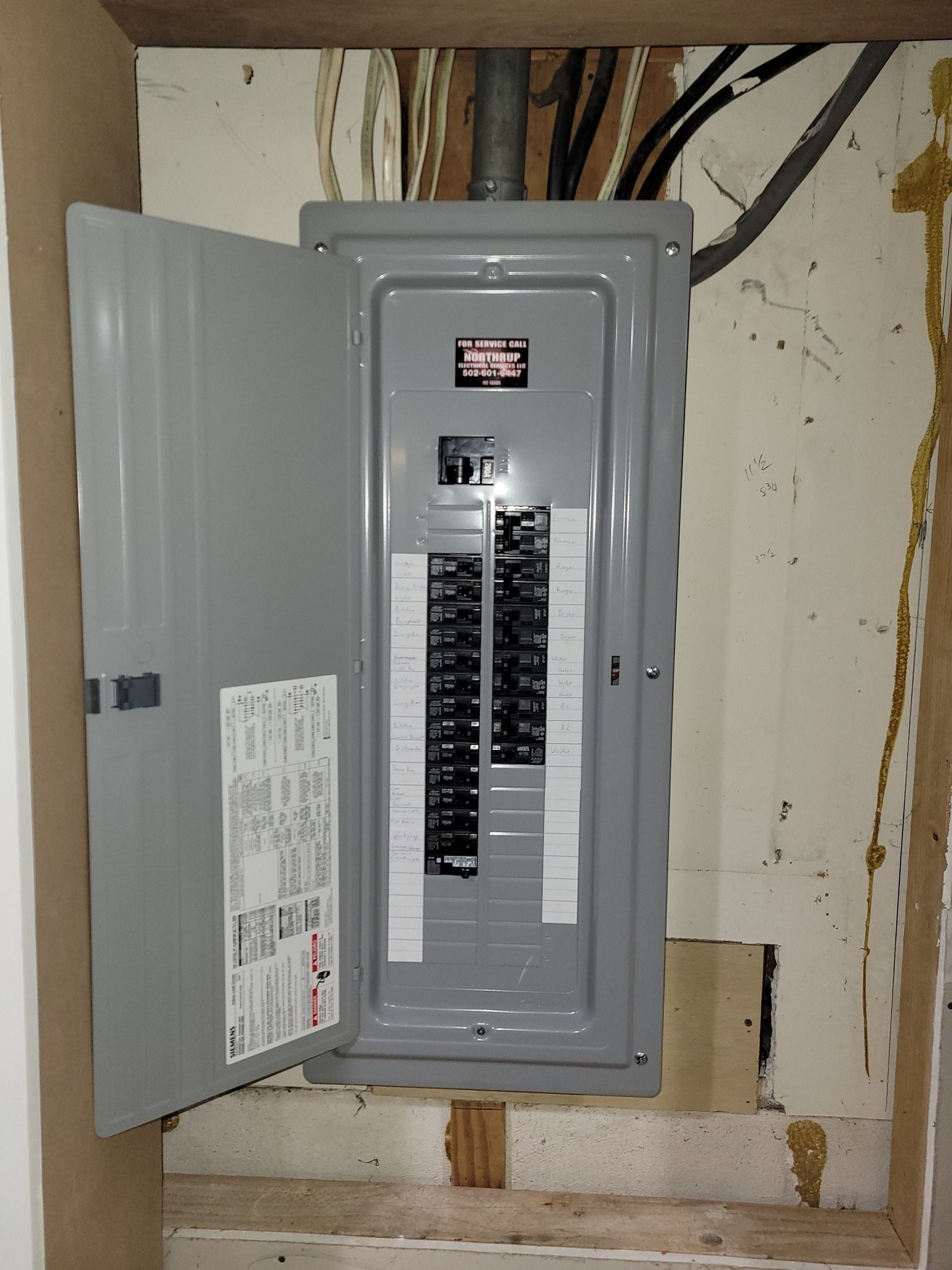 Gray electrical panel with open door, mounted in a wall. Wiring is visible.