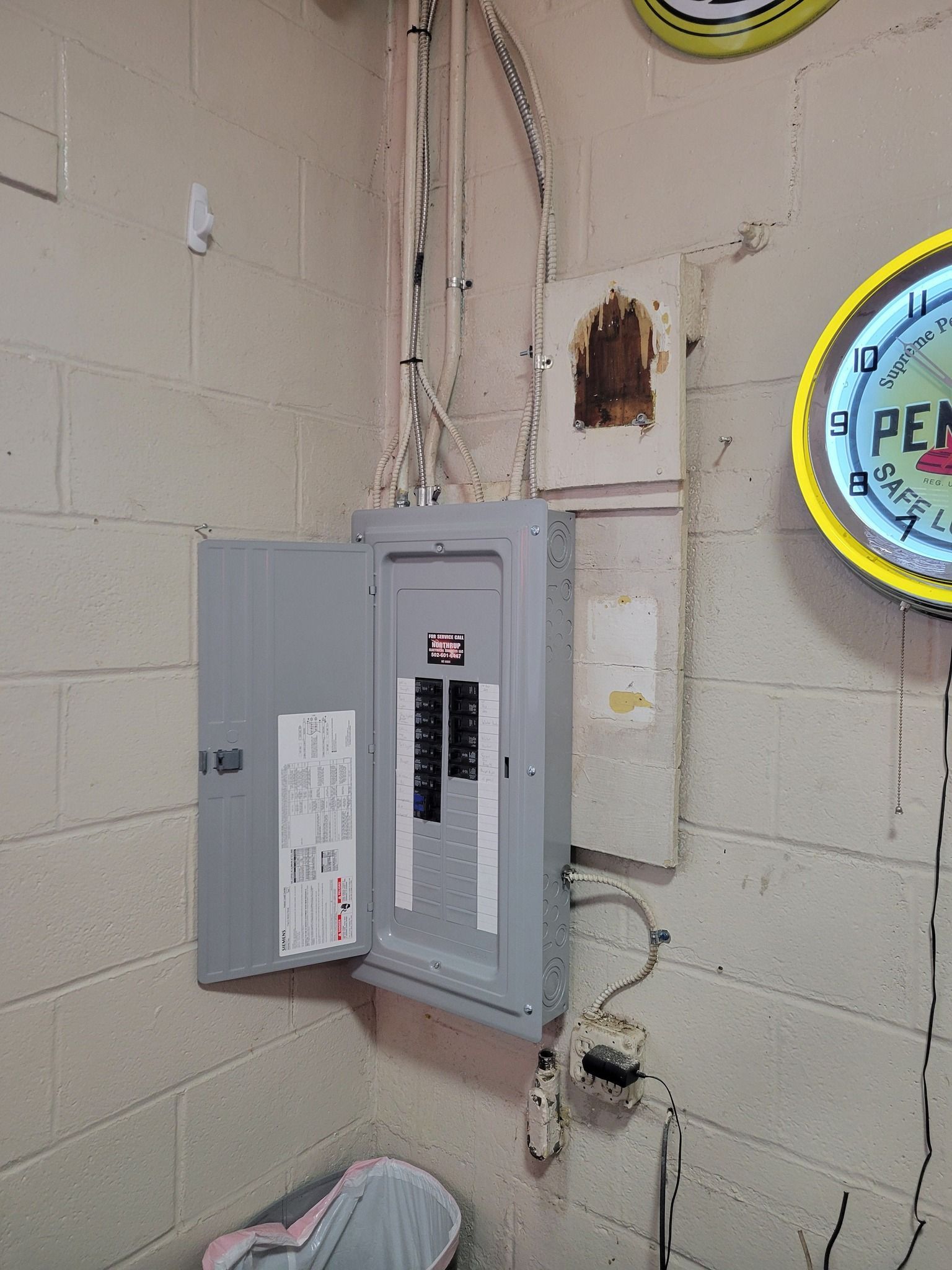 Electrical panel with open door on a concrete wall; wiring visible.