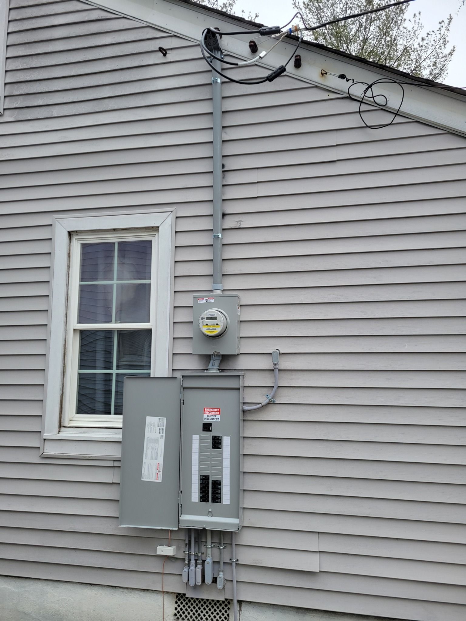 Exterior electrical panel and meter box mounted on a gray-sided house with a window.