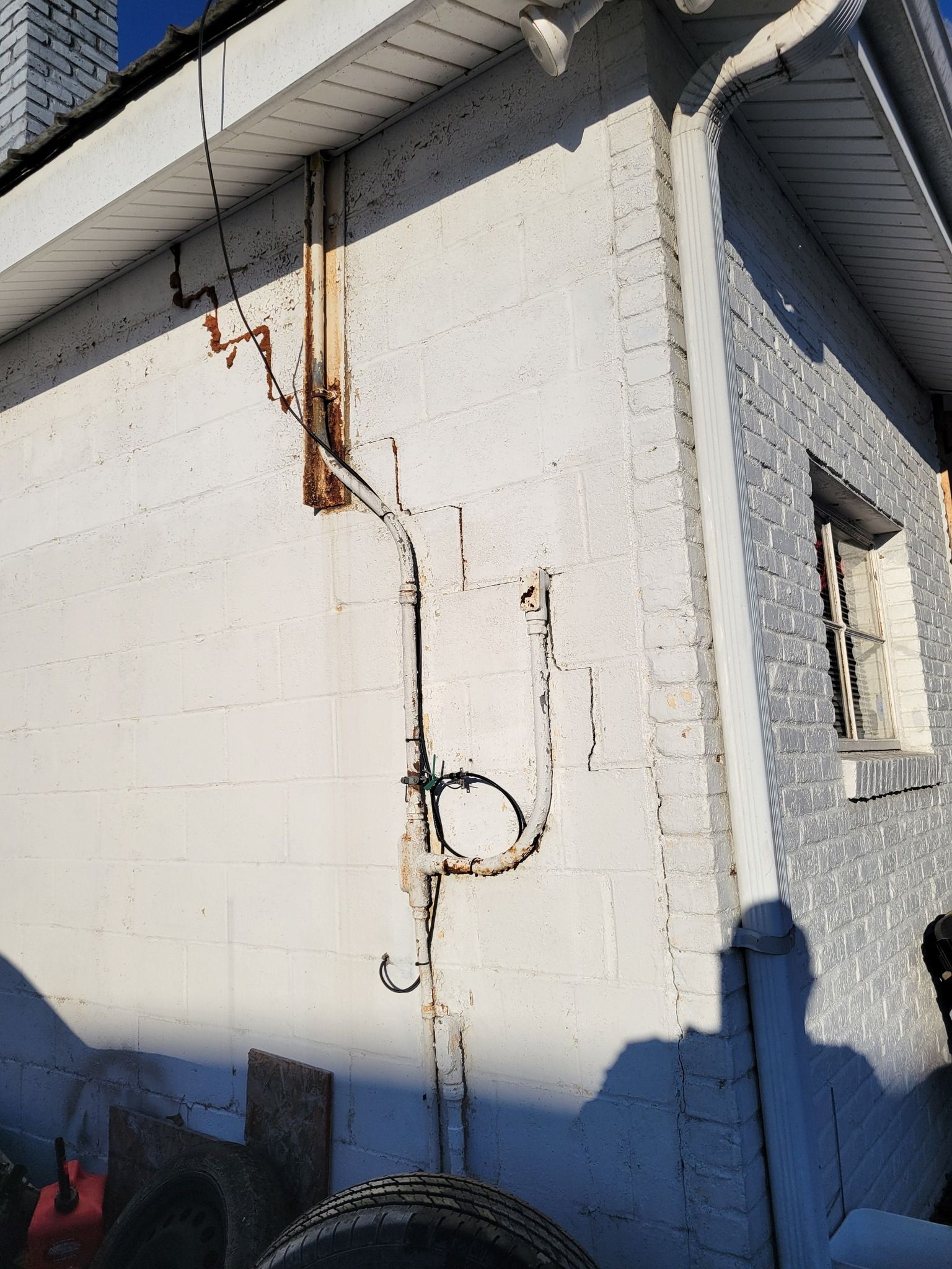 Exterior view of a white brick building with rusted pipes running along the wall.