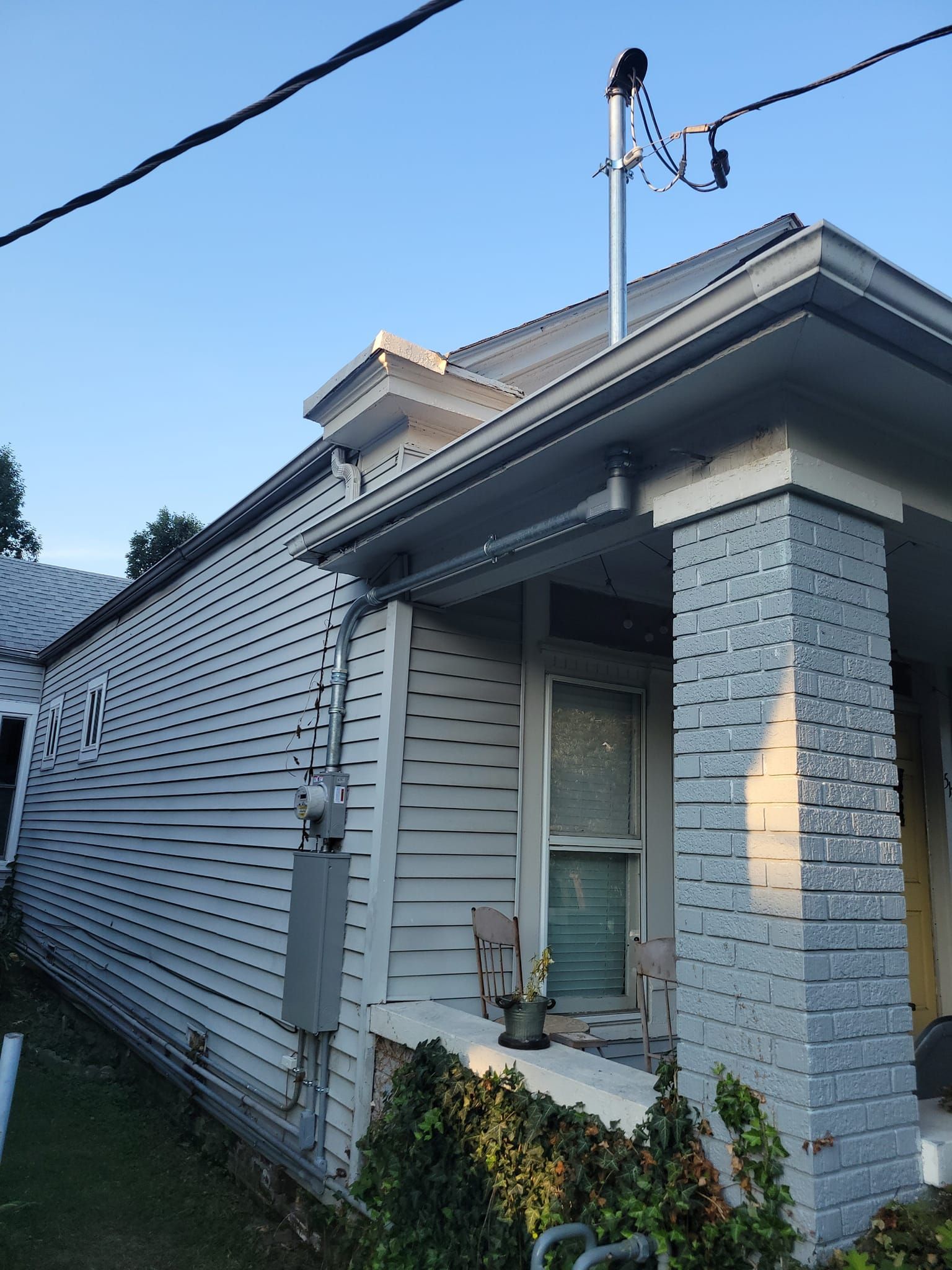Gray house with white siding and gray brick column; power lines overhead.