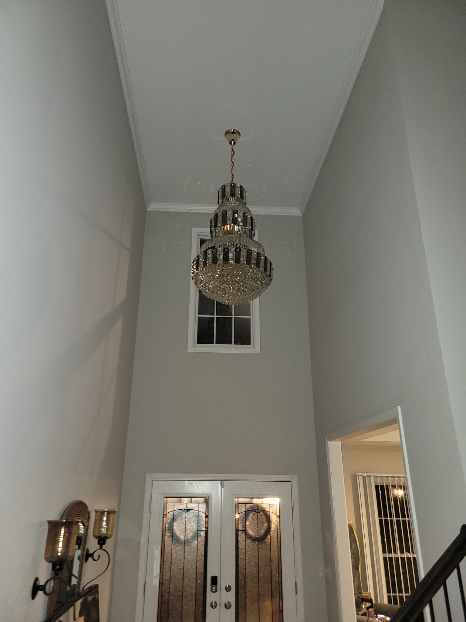 A tall entryway with a chandelier, front doors, and an open doorway to the right.