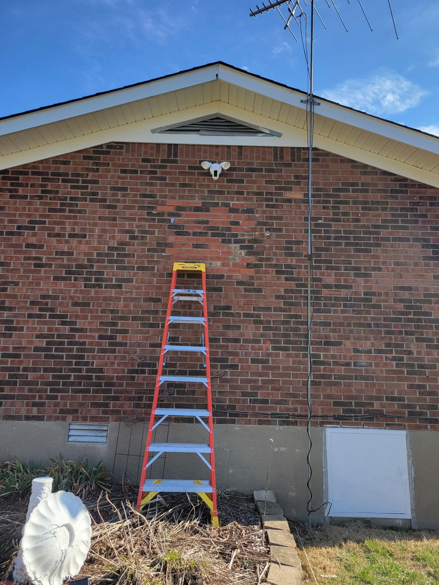 Ladder leaning against a brick building, antenna above.